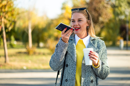 Portrait of modern businesswoman with sunglasses in stylish coat talking on mobile phone and...