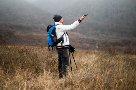 Worried and lost hiker in warm clothing is trying to find signal for his smartphone while hiking in nature. He is appearing confused about the route.の写真素材