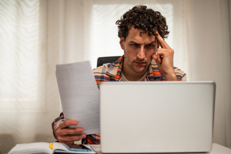 Worried businessman looking and analyzing documents while working on laptop at his home office.