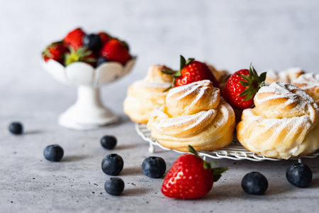 Delicious homemade profiteroles with powdered sugar, strawberries and blueberries. Gray background.の写真素材