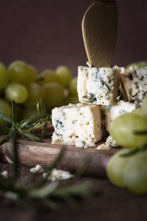 Blue cheese with a cheese knife on a wooden board. Against the background of grapes.の写真素材