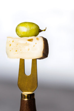 Camembert cheese with green grapes on a cheese fork.