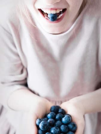 The girl eats fresh garden blueberries.の写真素材