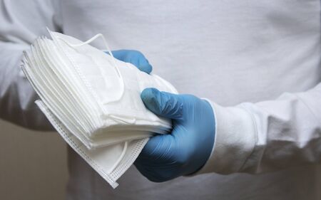 A volunteer wearing medical gloves holds a stack of disposable medical masks, during the coronovirus pandemic. The concept of mutual assistance and active citizenship. Close up.の写真素材