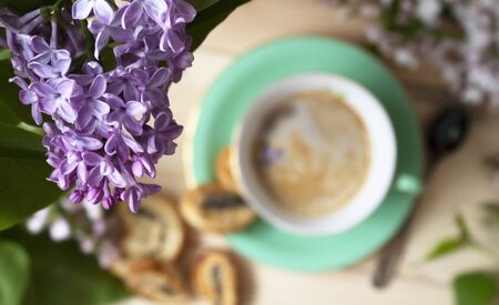 The flower arrangement is made of lilac flowers on a light wooden background with a Cup of coffee. Women's office Desk, stylized stock image, top view with empty space.の写真素材