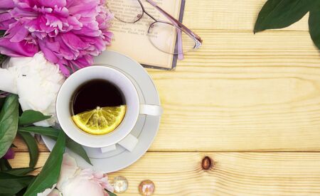 Summer layout with tea, book and peonies, on a wooden background. Rustic style. Layout with space for textの写真素材