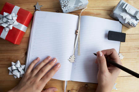 Womans hands writing on a notepad, christmas wish list on wooden table with festive ornamens and lights.の写真素材