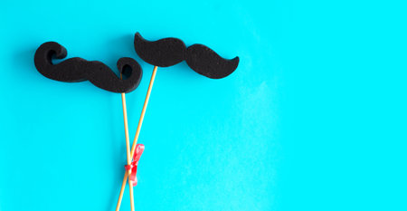 Black paper mustache on a stick on a blue background.
