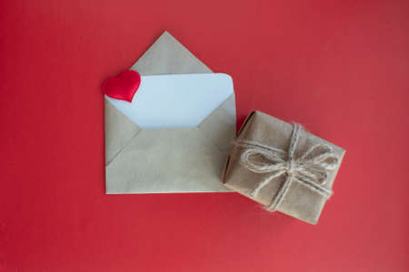 A gift and a paper envelope with a blank white mock-up of a note on a red background. The view from the top, the layout of greeting cardsの写真素材