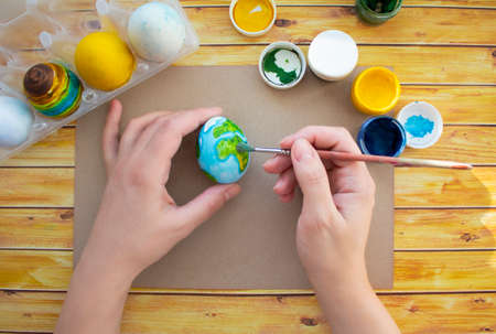 Easter egg decorating activities. Close-up image of a womans hands drawing a planet on an egg. Bottles with different colors.の写真素材