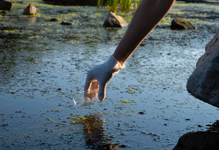 Samples of river water. The hand holds a chemical flask with a liquid, a lake or a river in the background.の写真素材