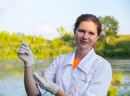 girl laboratory assistant looks at a sample of water in a test tube, recruited from the lake, the...
