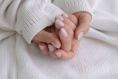 Well-groomed female hands, delicate manicure on a white knitted background, close-upの写真素材