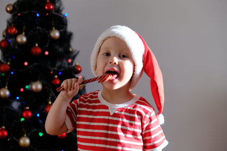 Baby in a Christmas hat, happy to eat caramel, Christmas tree in the background, the concept of...
