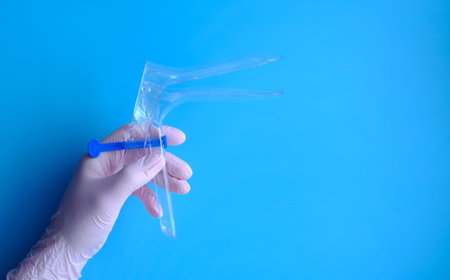 A hand in a pink rubber glove holds a gynecological mirror, a layout with copy space and space for text.の写真素材