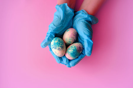 a hand in a blue rubber glove holds Easter eggs, a layout with copy space, an Easter