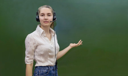 A young woman in a headset stands at a green board. distance learning conceptの写真素材