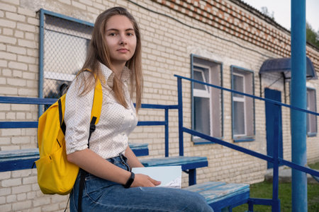 A student with a book sits on a bench on college grounds. Cute girl studying outdoorsの写真素材