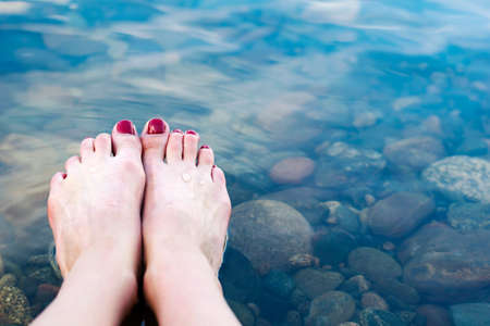Beautiful female feet with red nails on the background of water. Relaxing on the beach.の写真素材