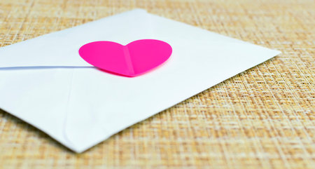 A white envelope with a pink heart. Love letter. Invitation to the wedding.