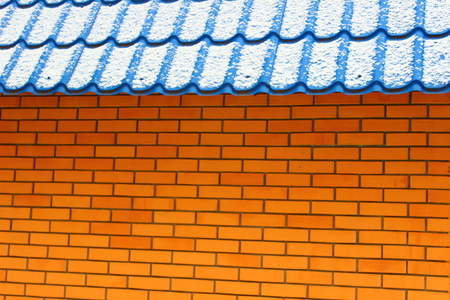 Orange brick wall and blue tin roof covered with snowの写真素材