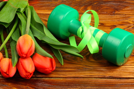 on a wooden board lay a bouquet of tulips and dumbbells for fitnessの写真素材