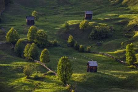 The idyllic scenery of the Bucovina region in Romania with green rolling hills and cottages in the sunset lightの写真素材