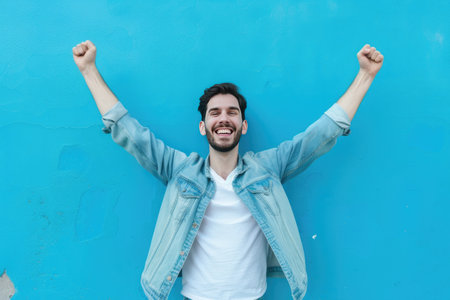 Portrait of a happy young man with arms raised on blue backgroundの素材