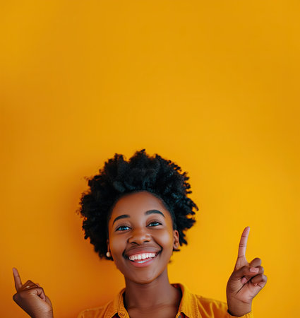 Happy young african american woman pointing finger up on yellow backgroundの素材