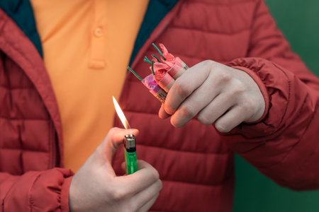 Man in Red Jacked Lighting Up Several Firecrackers in his Hand Using Gas Lighter. Guy Getting Ready...