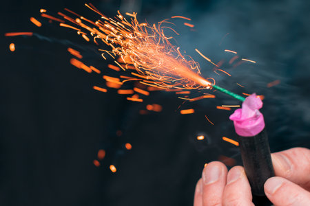 The Firecracker in a Hand. Man Holding a Burning Petard in His Hand. A Human with a Pyrotechnics that Burns with Sparks and Smoke Outdoorsの写真素材