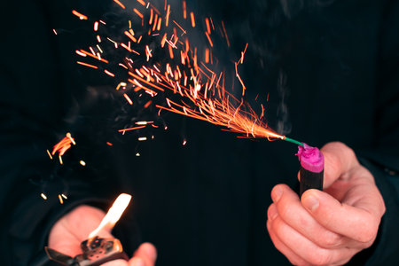 The Firecracker in a Hand. Man Holding a Burning Petard in His Hand. A Human with a Pyrotechnics that Burns with Sparks and Smoke Outdoorsの写真素材