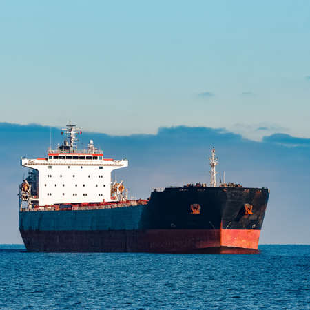 Black cargo ship moving in still Baltic sea water. Riga, Europeの写真素材