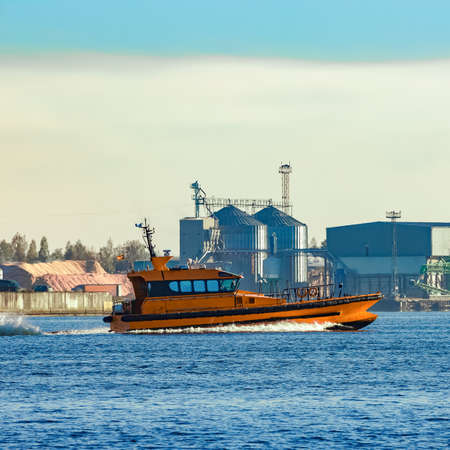 Orange pilot ship sailing past the factory in Latviaの写真素材