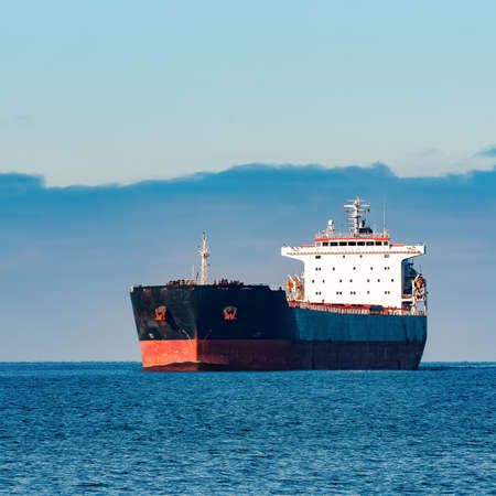 Black cargo ship moving in still Baltic sea water. Riga, Europeの写真素材