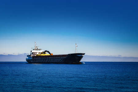 Black Sailing Bulk Carrier. Cargo Ship with Long Reach Excavator Moving in Still Water at Sunny Day by the Seaの写真素材