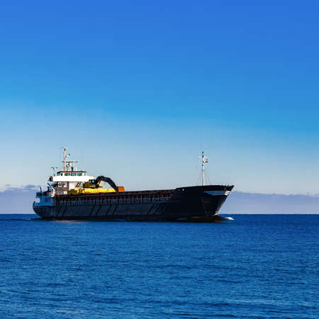 Black Sailing Bulk Carrier. Cargo Ship with Long Reach Excavator Moving in Still Water at Sunny Day by the Seaの写真素材