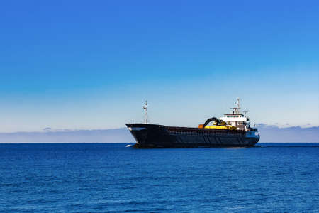 Black Sailing Bulk Carrier. Cargo Ship with Long Reach Excavator Moving in Still Water at Sunny Day by the Seaの写真素材