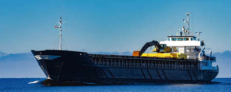 Black Sailing Bulk Carrier. Cargo Ship with Long Reach Excavator Moving in Still Water at Sunny Day...