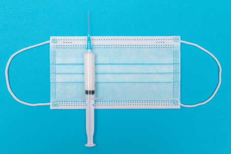 A Syringe and Face Mask on Blue Table - Top View. Syringe is Prepared for Vaccination or Injection. Medical Experiment. Blue Disposable Medical Mask. Virus protection - Flat Layの写真素材