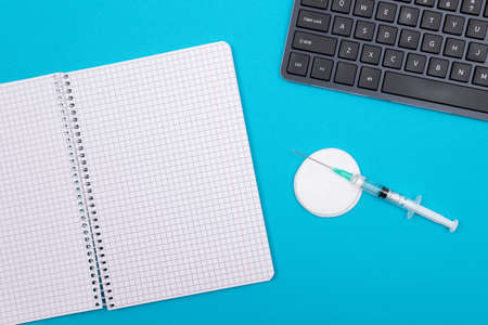 Vaccination, Immunology or Revaccination Concept - A Medical Syringe Lying on Blue Table in Doctors Office in a Hospital or Clinic. Opened Blank Notepad - Mock Up with Copy Spaceの写真素材