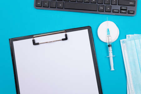 Vaccination, Immunology or Revaccination Concept - A Medical Syringe Lying on Blue Table in Doctors Office in a Hospital or Clinic. Black Clipboard with Sheet of Paper - Mock Up with Copy Spaceの写真素材