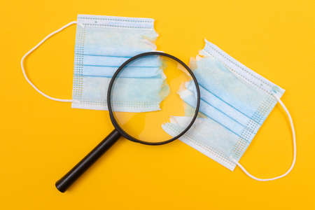 Anti Mask Concept - Torn Medical Face Mask and Magnifier Lying on Yellow Background. Pandemic and...