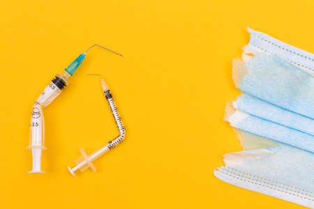 Anti Vaccine Movement and Anti Mask Concept - Broken Medical Syringe and Torn Medical Face Mask Lying on Yellow Background. Pandemic and Lockdown End - Top View, Flat Layの写真素材