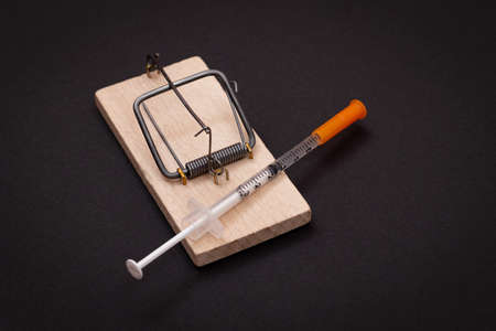 Drug Addict, Heroin Hazard or Dose Trap Concept - Disposable Insulin Syringe with Drug Dose Inside Lying in Wooden Mousetrap on Black Backgroundの写真素材