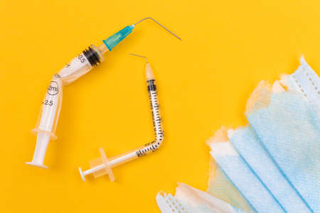 Anti Vaccine Movement and Anti Mask Concept - Broken Medical Syringe and Torn Medical Face Mask Lying on Yellow Background. Pandemic and Lockdown End - Top View, Flat Layの写真素材