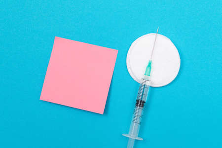 Vaccination, Immunology or Revaccination Concept - A Medical Disposable Syringe Lying on Blue Table in Doctors Office in a Hospital or Clinic. Blank Pink Sticky Note - Mock Up with Copy Spaceの写真素材