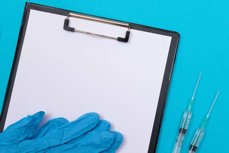 Vaccination, Immunology or Revaccination Concept - Two Medical Syringe Lying on Blue Table in Doctors Office in a Hospital or Clinic. Black Clipboard with Sheet of Paper - Mock Up with Copy Spaceの写真素材