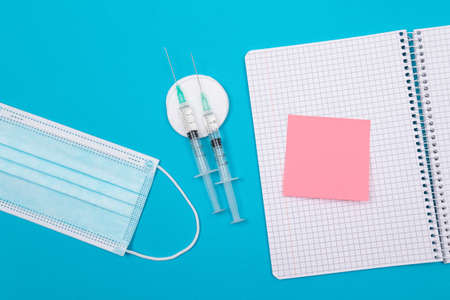 Vaccination, Immunology or Revaccination Concept - Two Medical Disposable Syringe Lying on Blue Table in Doctors Office in a Hospital or Clinic. Blank Pink Sticky Note - Mock Up with Copy Spaceの写真素材