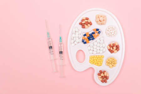 Global Pharmaceutical Industry and Medicinal Products - Different Colored Pills, Tablets and Capsules on White Art Palette with Syringe Lying on Pink Background, Flat Layの写真素材